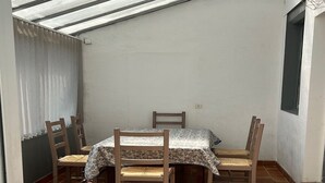 Un petit espace repas fermé, comprenant une table et quatre chaises, une fenêtre avec des rideaux et un sol carrelé.