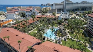A resort with a central pool surrounded by palm trees, multiple buildings with red roofs, and a view of the ocean. - LOCATION LOCATION LOCATION 2 (Cabo San Lucas)