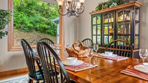 Une salle à manger avec une table en bois, des chaises noires et un lustre. On y trouve également un buffet aux portes vitrées où sont exposés des objets décoratifs.
