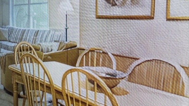 A dining area with a wooden table and chairs, framed artwork on the wall, and a window with blinds.