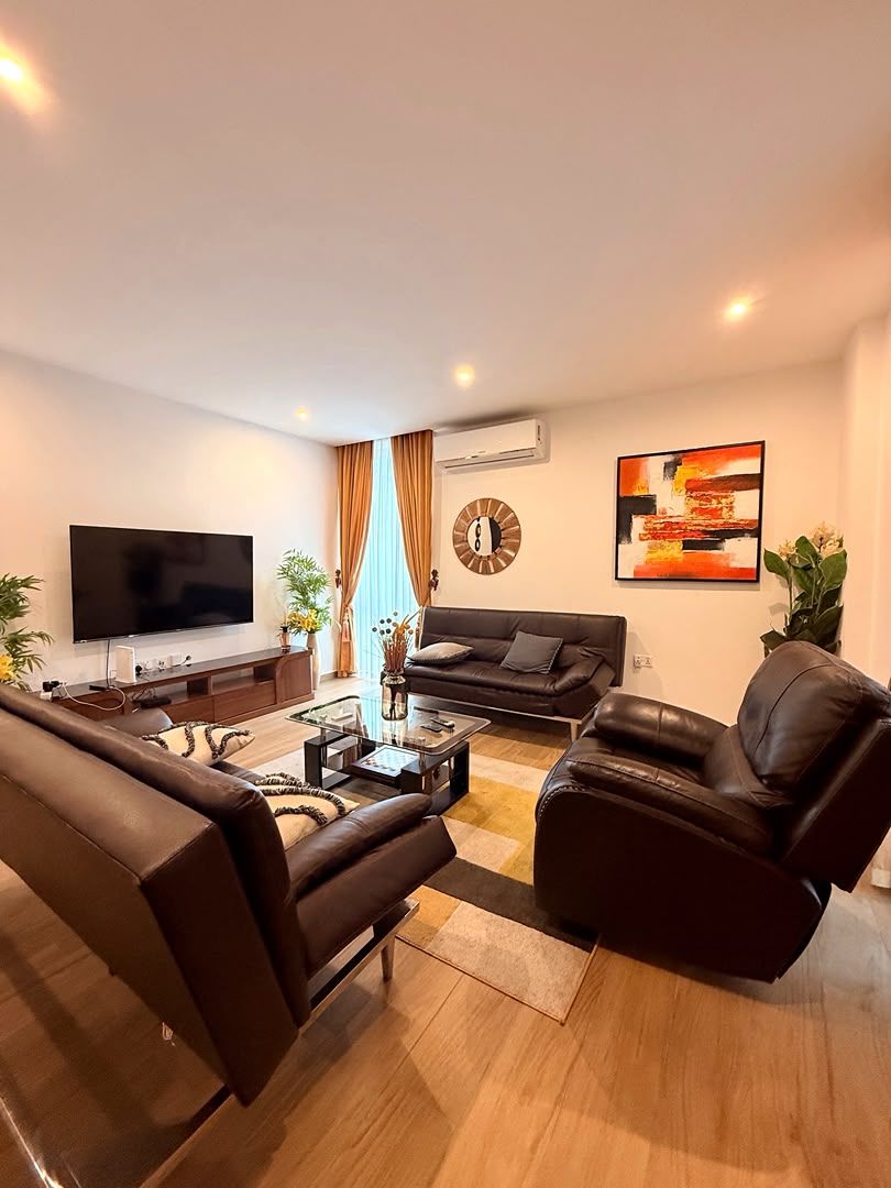 Una sala de estar moderna con un televisor de pantalla plana, sofás de cuero, una mesa de centro y un gran ventanal con cortinas.
