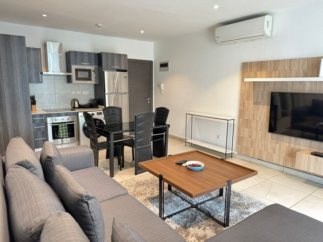 Un salon moderne avec un canapé, une table basse et un téléviseur. Il y a également un coin cuisine équipé d’un four à micro-ondes, d’une cuisinière et de chaises.