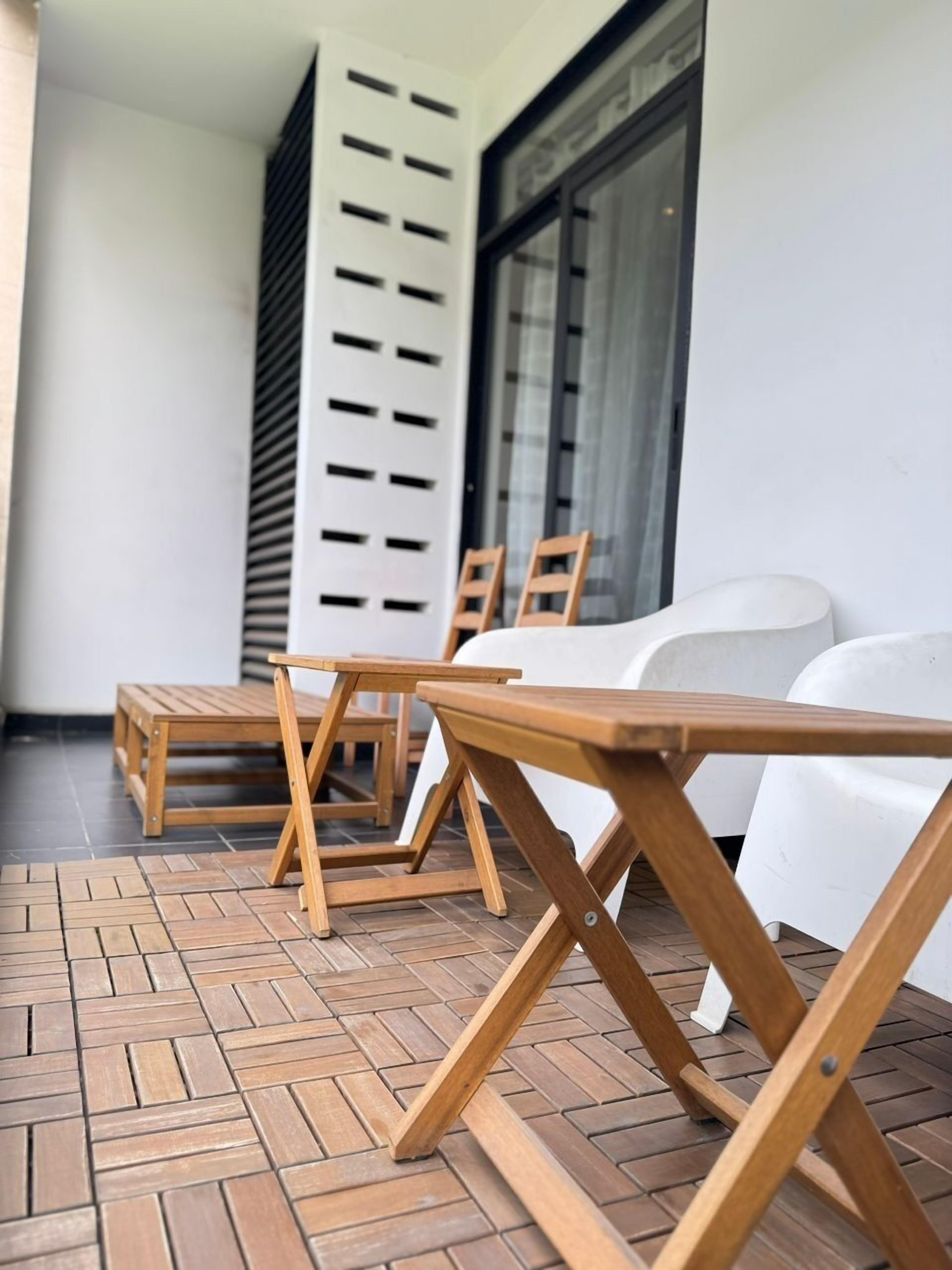 A patio area with wooden tables and chairs, a white sofa, and a large window with blinds.