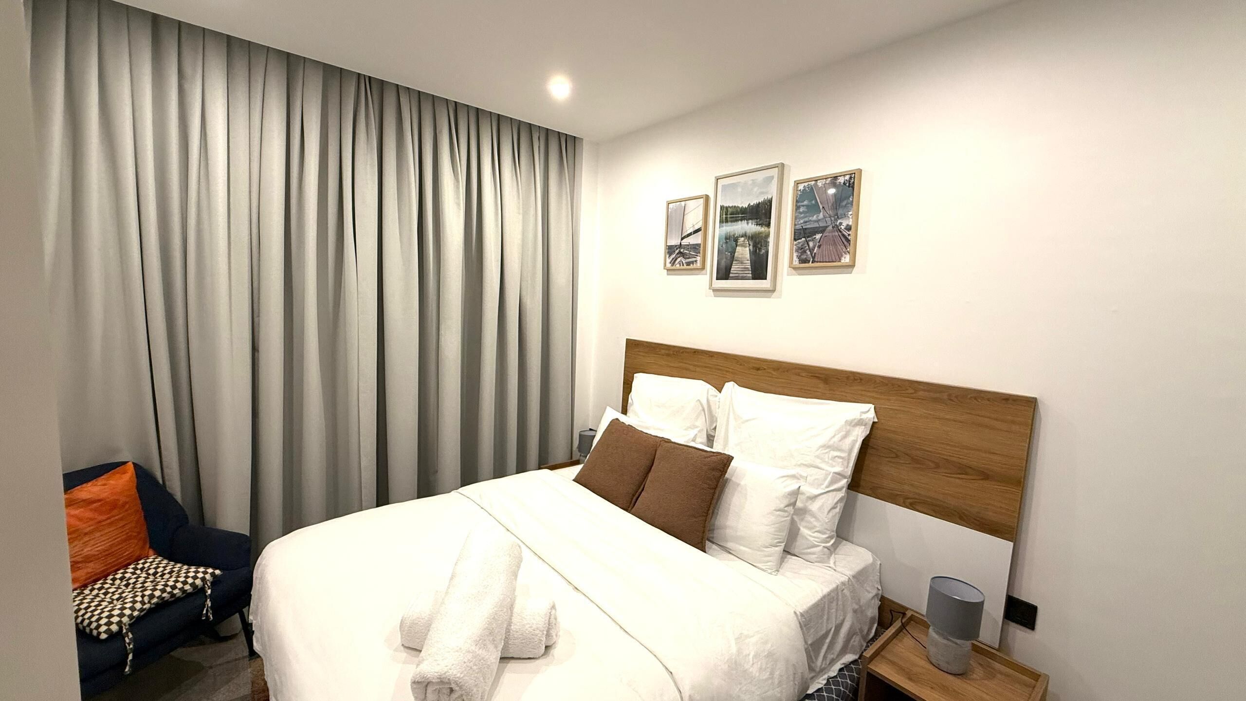 A hotel room with a large bed, a wooden headboard, a nightstand, a lamp, and a chair with a patterned cushion.