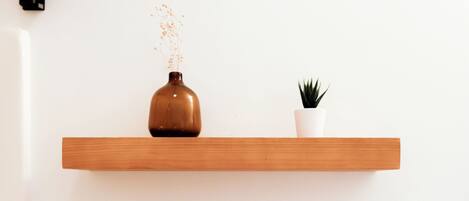 Deux étagères en bois adossées à un mur blanc, l’une avec un vase marron et une petite plante, et l’autre avec des serviettes blanches pliées.