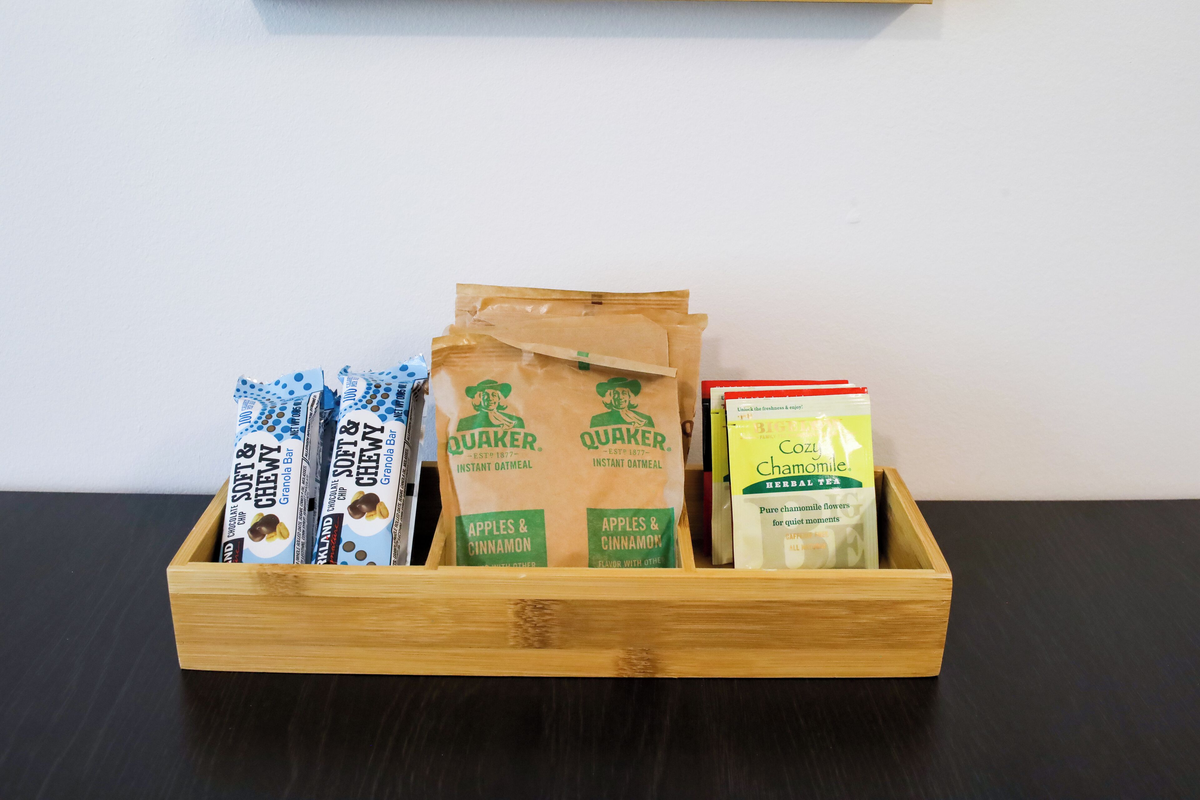A wooden box containing instant oatmeal packets, Quaker brand, and a box of Chomolilly tea.