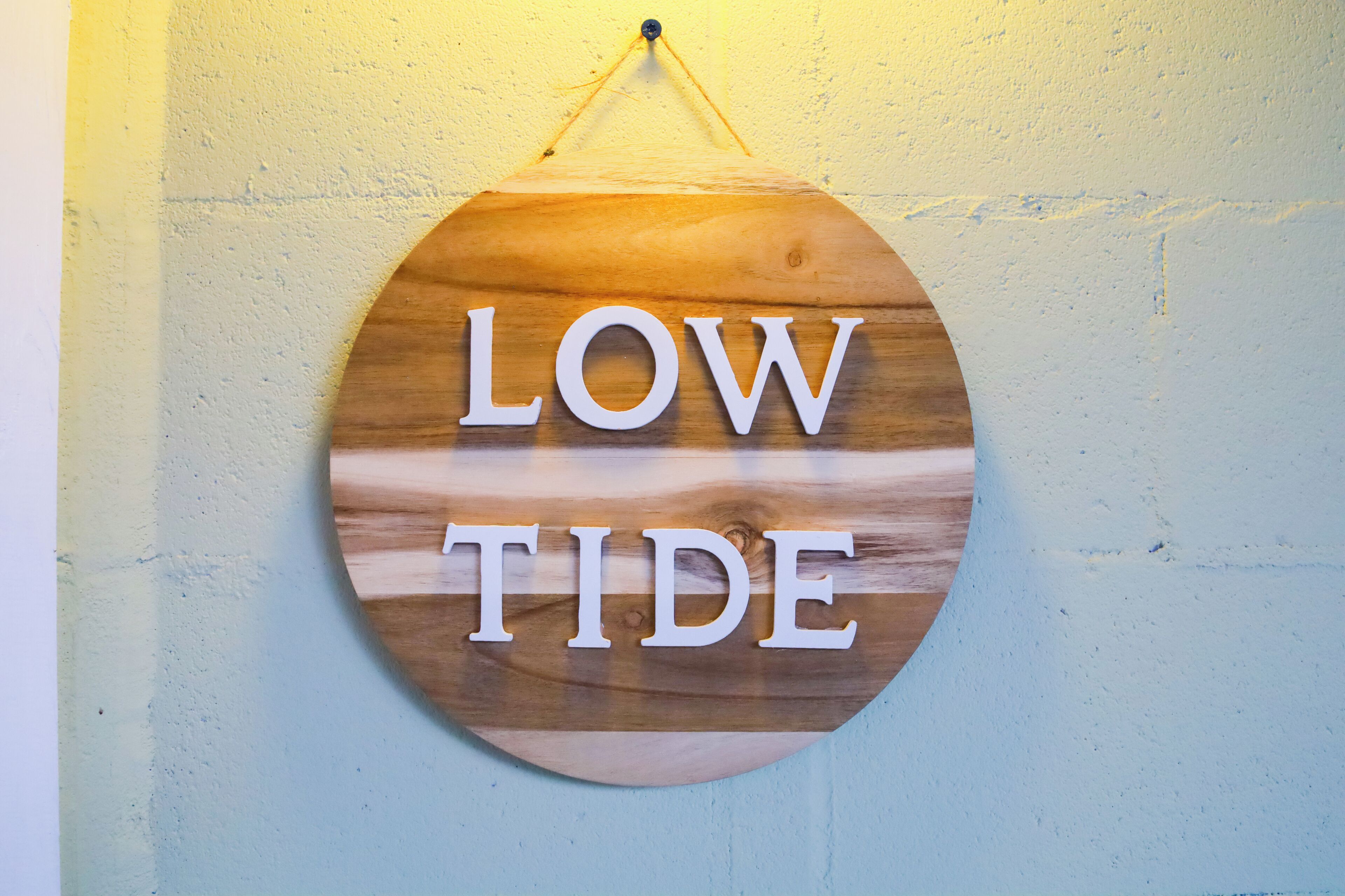 Un letrero circular de madera con la inscripción 'LOW TIDE' sobre una pared con textura.