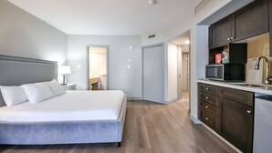 Ein modernes Hotelzimmer mit einem großen Bett, einer Küchenzeile und einem durchgegangenes Badezimmertür sichtbaren Bad.
