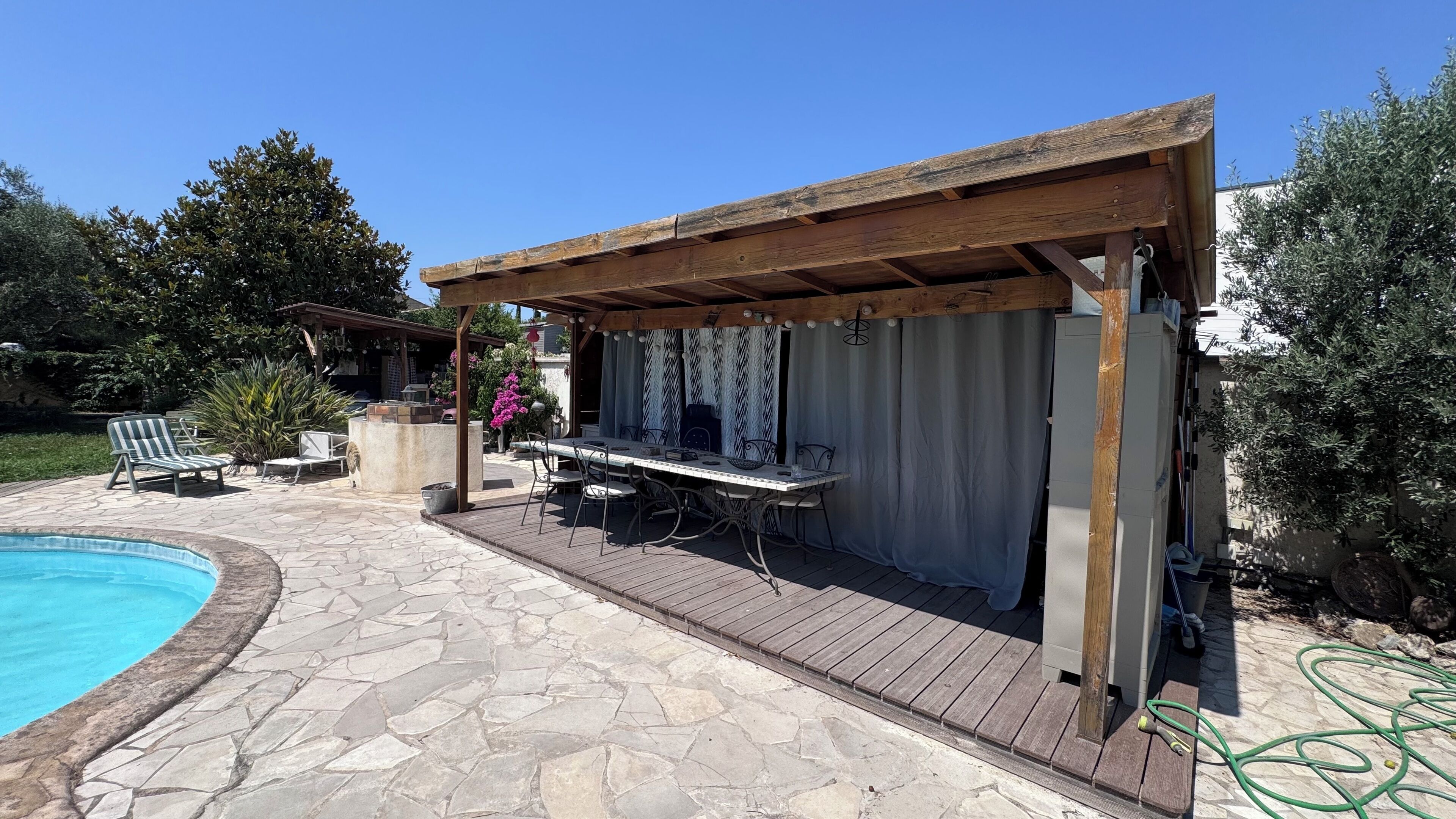 A covered outdoor patio with a pool, stone flooring, and a wooden pergola.