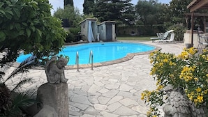 En swimmingpool med stentile, omgivet af grøn vegetation og et pergola