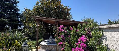 A stone patio with a pergola, outdoor seating, and vibrant bougainvillea flowers.