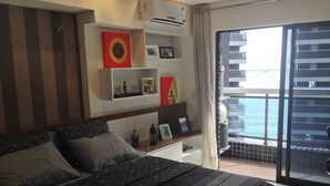 Una habitación de hotel con cama, mesita de noche, ventana con vistas al mar y balcón.