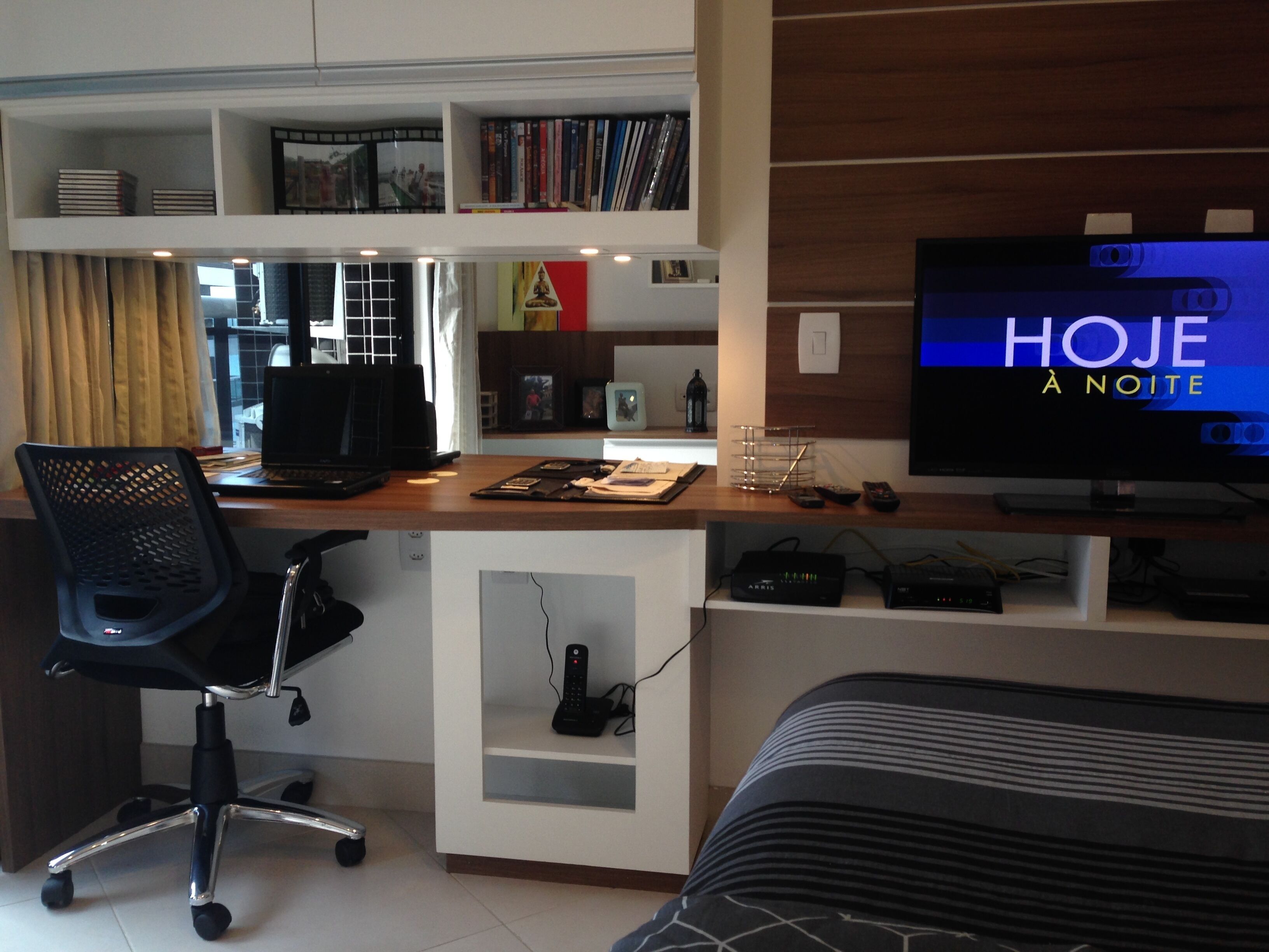 Et moderne hotelværelse med skrivebord, computer og fjernsyn, der viser "HOJE À NOITE".