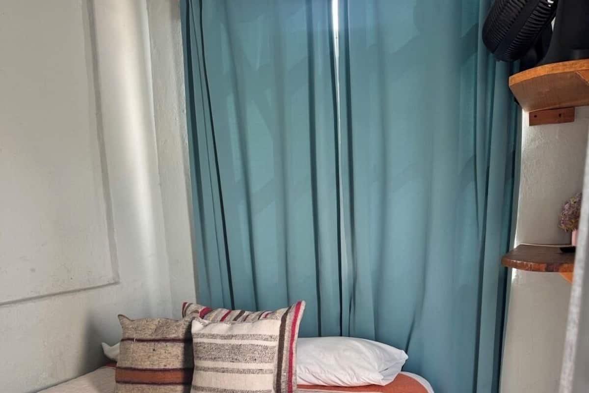 Ein Schlafzimmer mit einem Bett, Kissen, einem Nachttisch, einer Wandheizung und einem Vorhang.