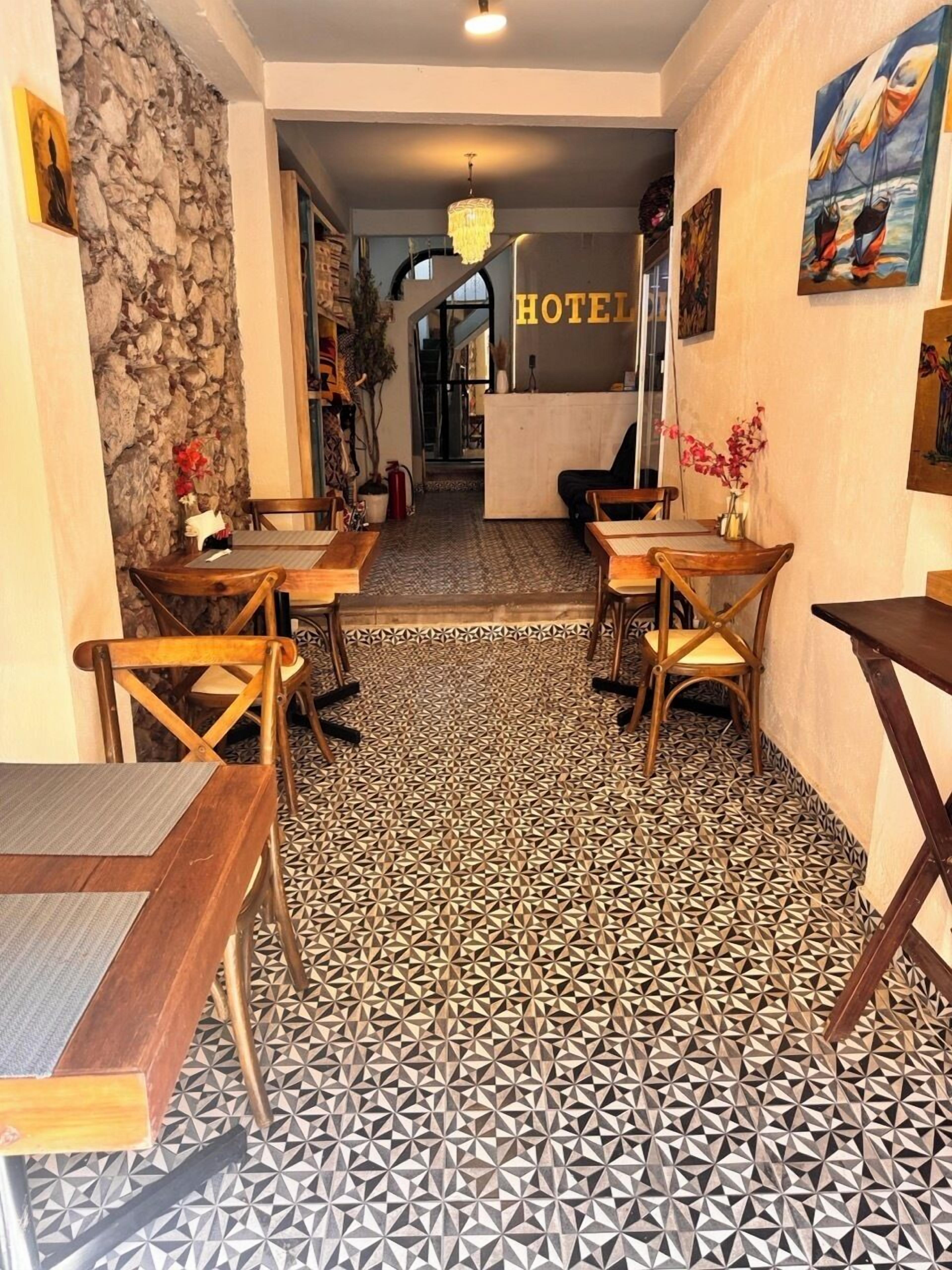 A hotel lobby with a geometric patterned floor, wooden tables and chairs, a stone wall, and a 'HOTEL' sign.