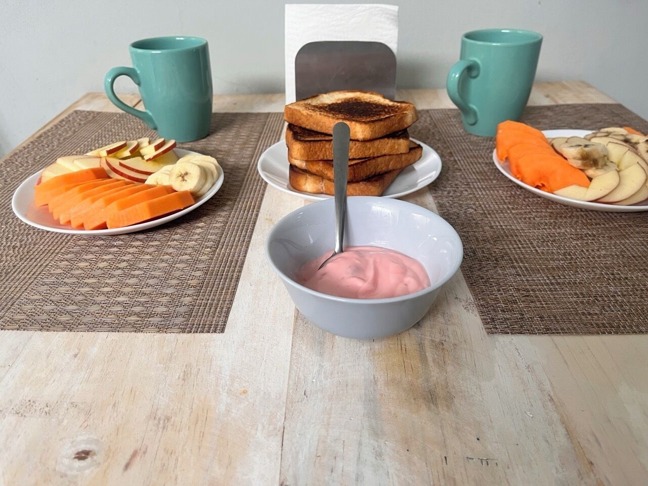 A breakfast setting with toast, fruit, and a bowl of pink yogurt.