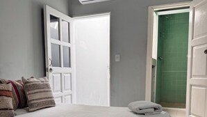 Une chambre à coucher avec un lit, des oreillers, un appareil de climatisation et une porte de salle de bain recouverte de carreaux verts.
