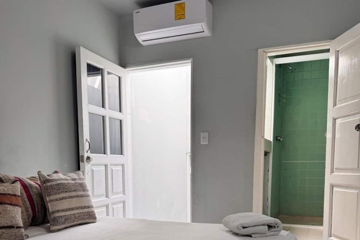 Ein Schlafzimmer mit Bett, Kissen, einer Klimaanlage und einer türförmigen Badezimmertür mit grünen Fliesen.