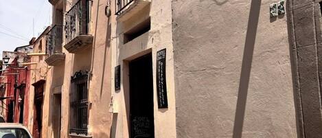 A narrow street with a stone-paved sidewalk, a parked car, and a building with a sign indicating a hotel named 'Hotel Casa 22.'