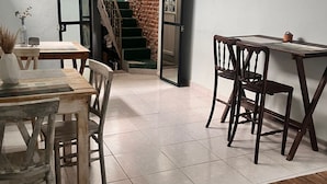 Un coin repas avec une table et des chaises en bois, un escalier menant à un mur en briques, et une vue à travers une porte ouverte.
