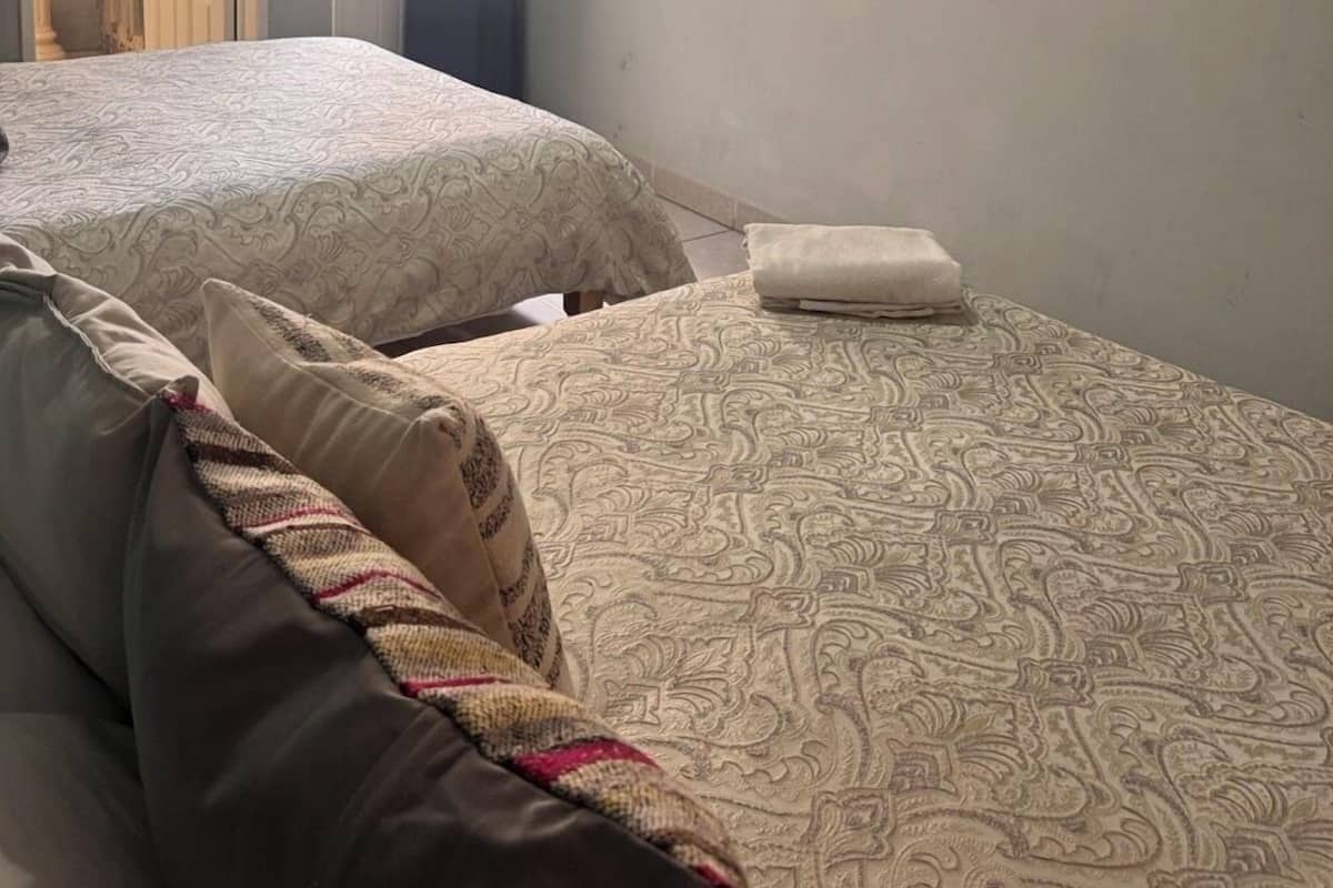 Ein Zimmer mit zwei Betten, einem an der Wand befestigten Flachbildfernseher und einem durch eine geöffnete Tür einsehbaren Badezimmer.
