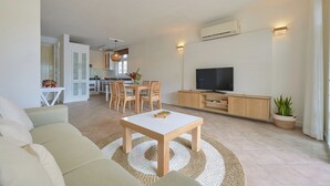 A modern living room with a sofa, a coffee table, a TV, and a dining area with chairs and a table.