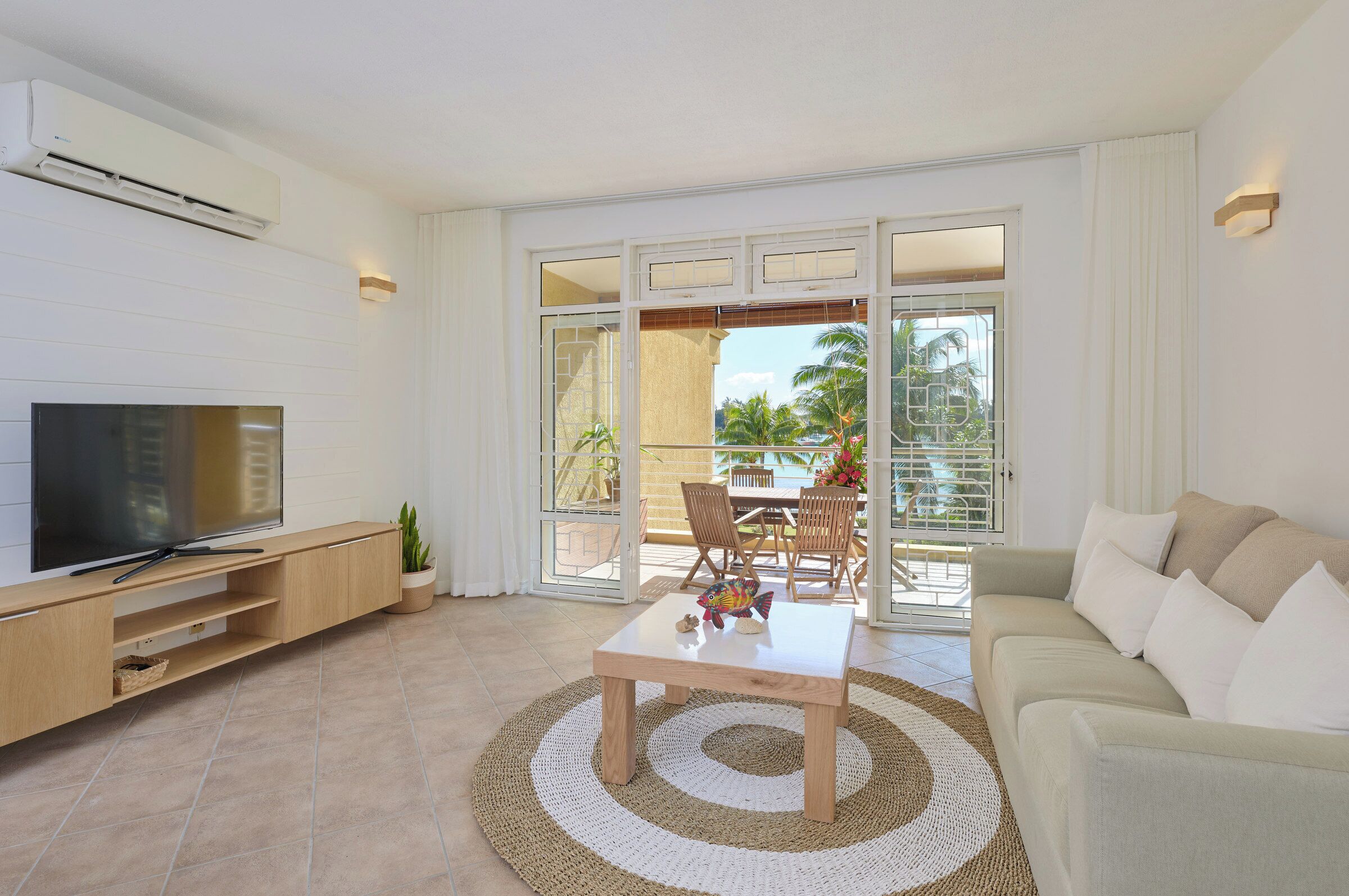 A modern living room with a flat-screen TV, wooden entertainment unit, a coffee table, and a beige sofa.