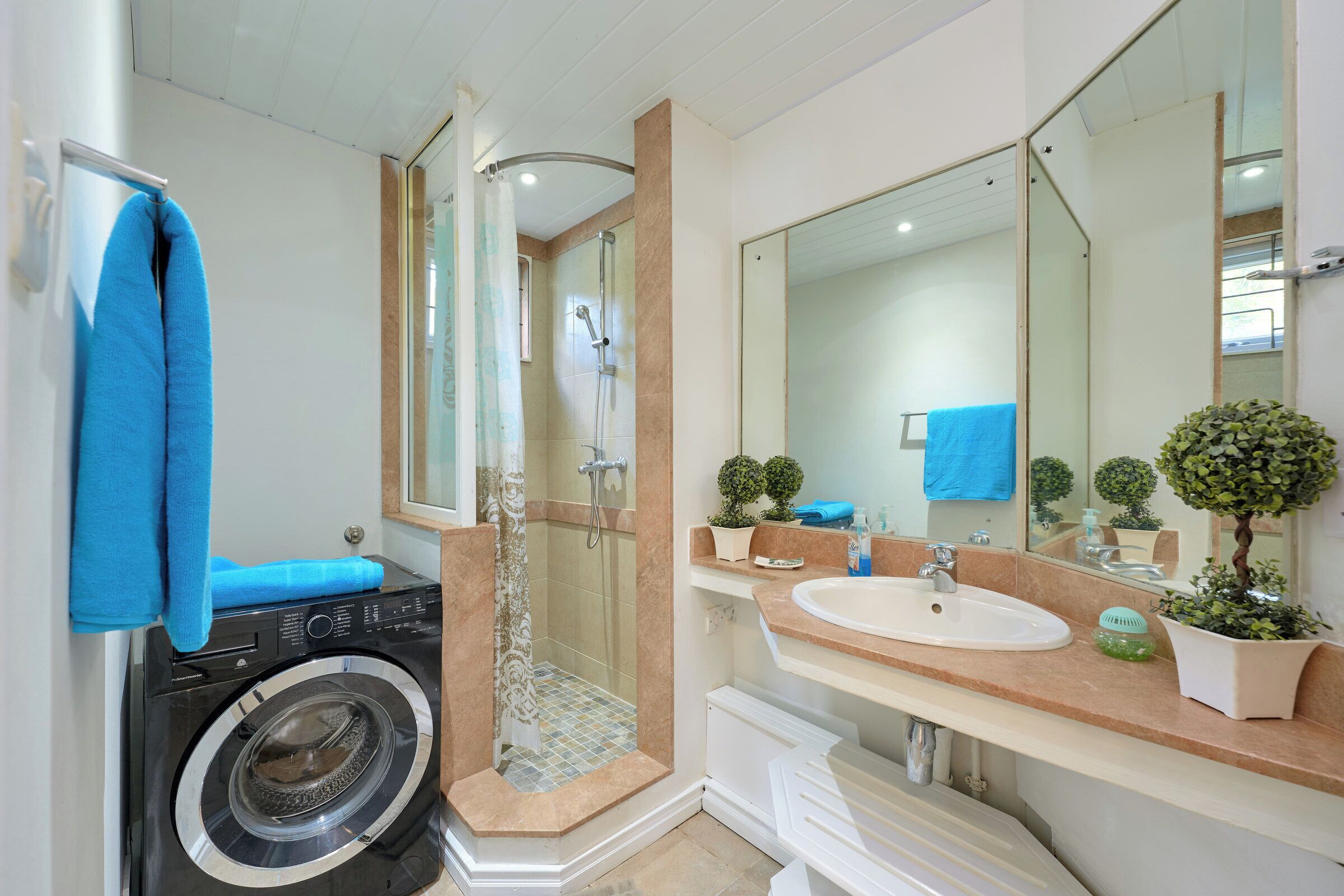 A bathroom with a washing machine, a shower, a sink, and a large mirror.