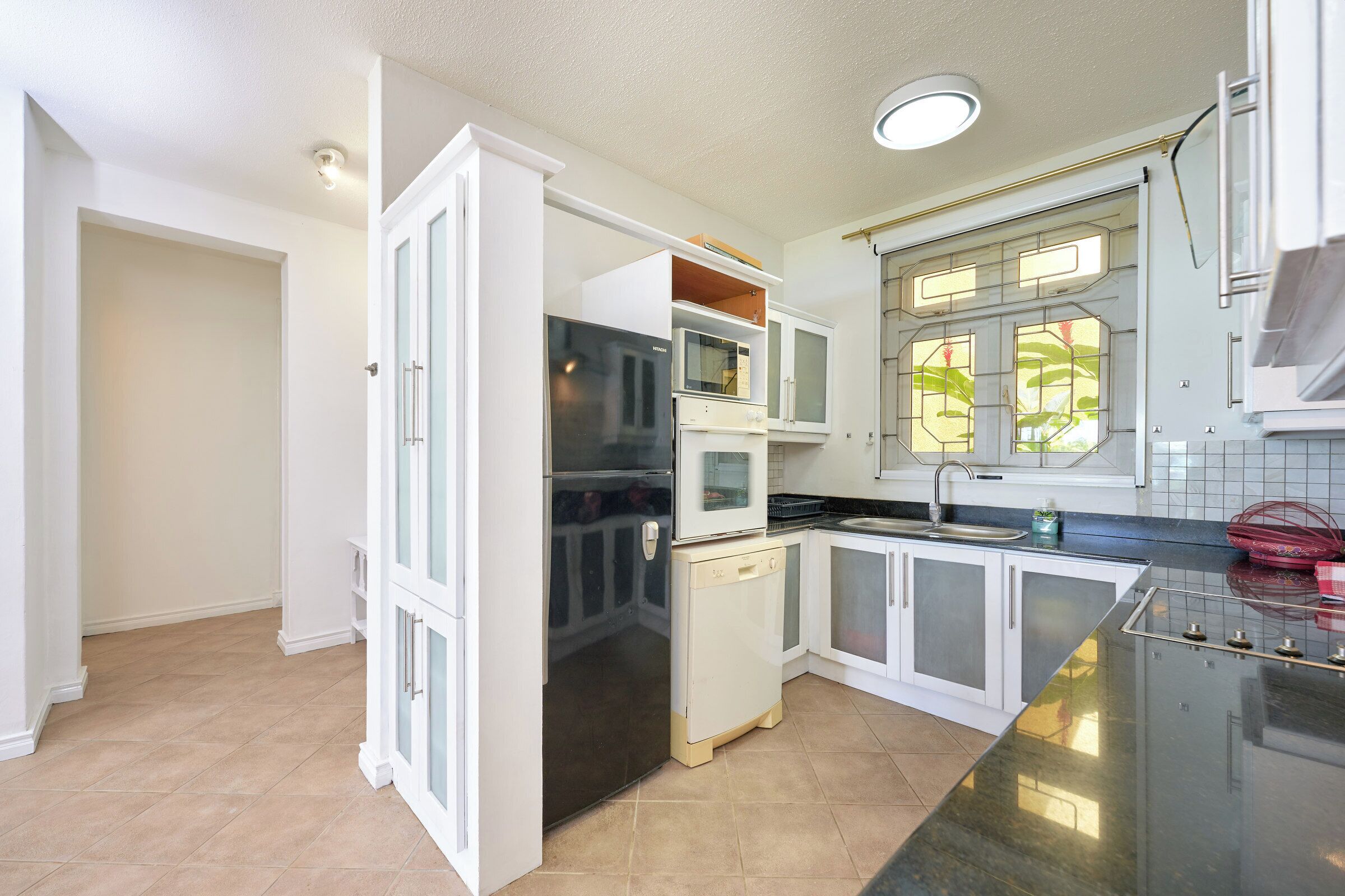 A modern kitchen with white cabinetry, a black refrigerator, and a window with green foliage.
