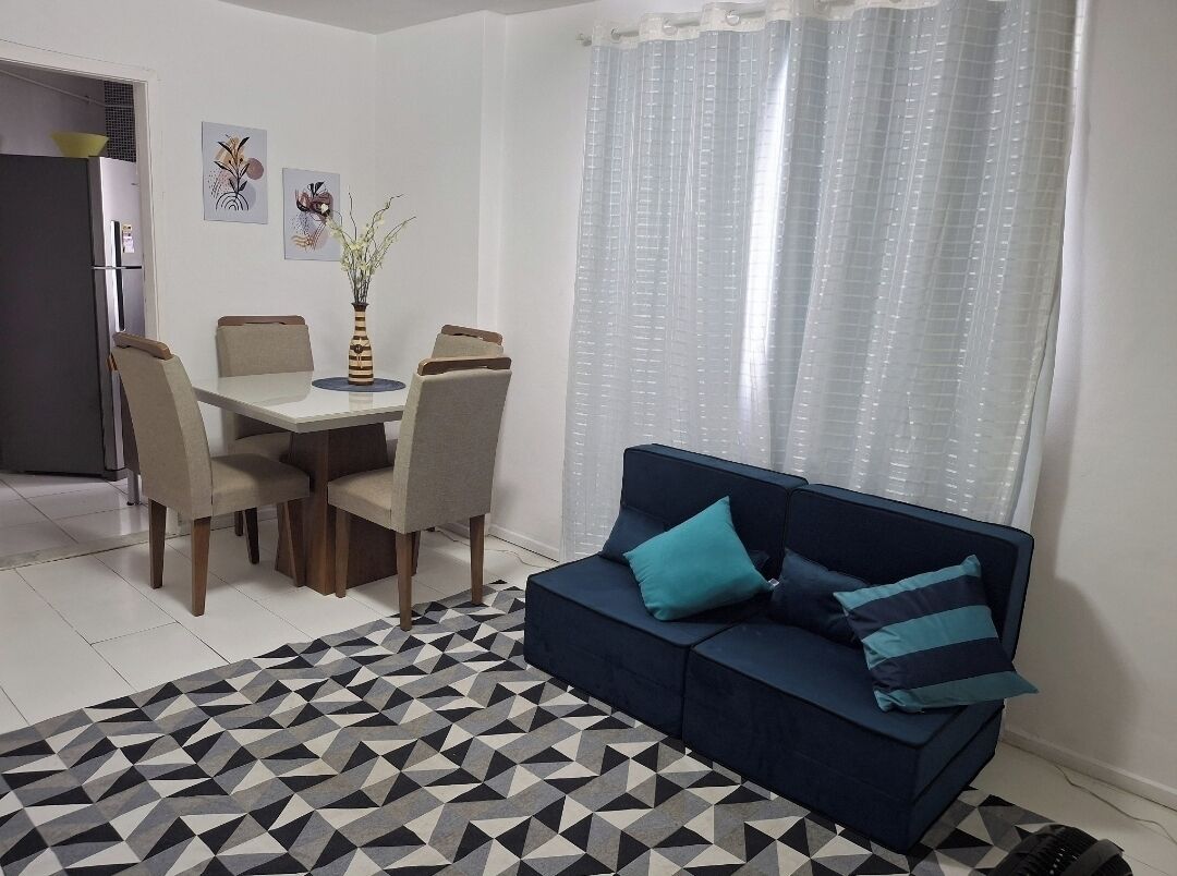 Uma área de refeições com mesa, cadeiras, um sofá e um tapete estampado.