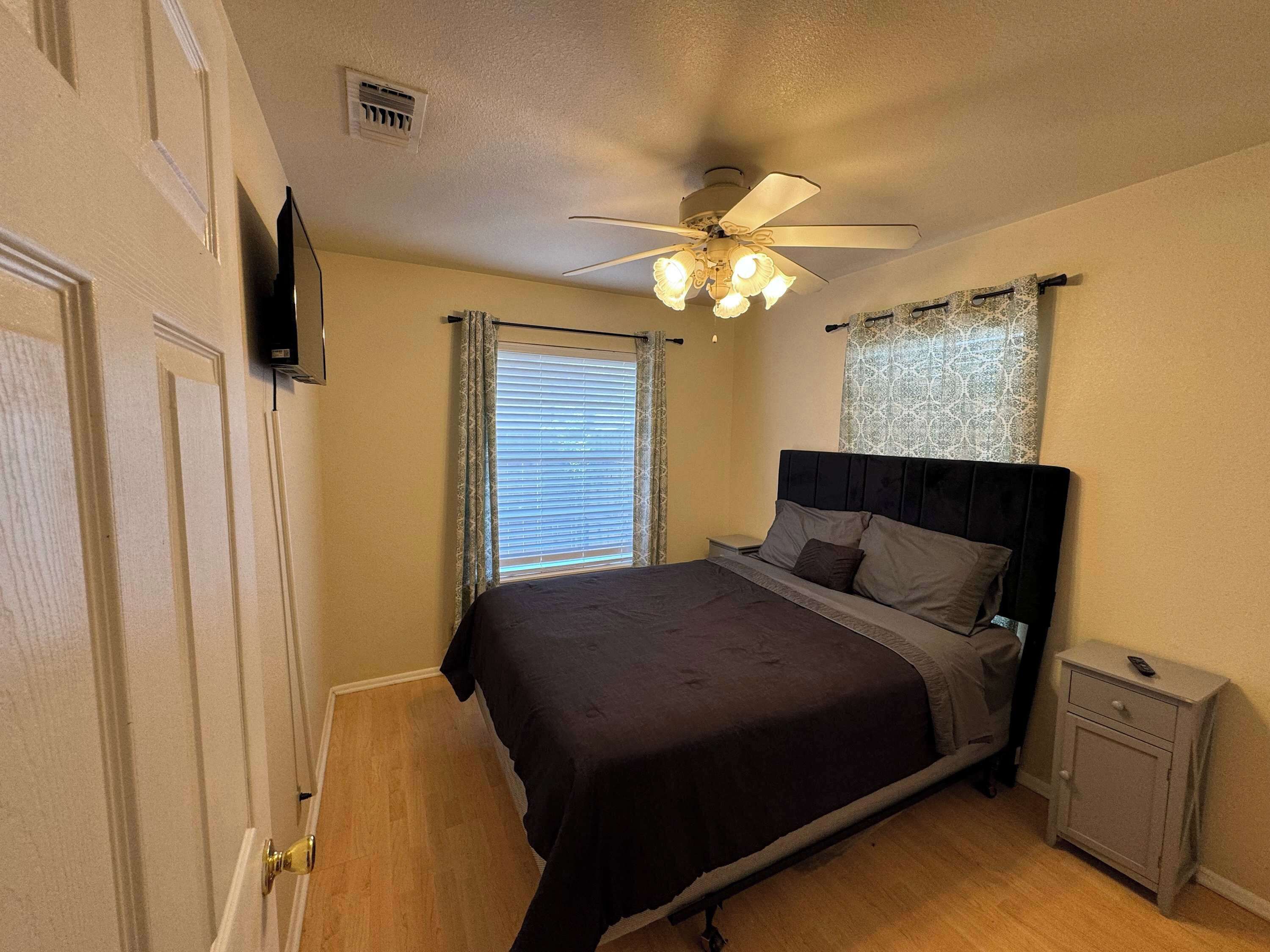 Ein Schlafzimmer mit Bett, Nachttisch, Deckenventilator und Fenster mit Jalousien.