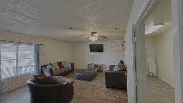 A spacious living room with a large sectional sofa, a round ottoman, and a flat-screen TV mounted on the wall. - Latigo Haven - 7 Mins to Lackland (San Antonio)