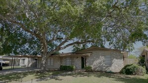 A stone building with a covered porch, surrounded by a grassy area and a tree. - Latigo Haven - 7 Mins to Lackland (San Antonio)