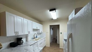 A kitchen with white cabinets, a marble countertop, a coffee maker, a sink, and a refrigerator. - Latigo Haven - 7 Mins to Lackland (San Antonio)