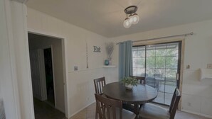 A dining area with a round table, four chairs, a ceiling light fixture, a window with a view, and a door leading to another room. - Latigo Haven - 7 Mins to Lackland (San Antonio)