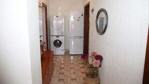 Un passadís estret amb una rentadora i un frigorífic. Hi ha un mirall a la paret i un ram de flors a terra.