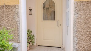 Een beige deur met een ruit en een kleine potplant ernaast.