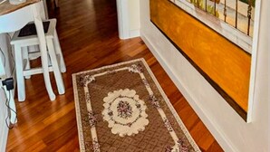 A hallway with a wooden floor, a white chair, a desk with a lamp, and a painting of a garden with a balcony. - B&B by Family L&G - Vibo Marina (Vibo Marina)