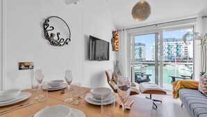 A dining area with a table set for four, a sofa, and a view of a marina through large windows. - On the Water 7 Free Parking By My Getaways (Brighton)