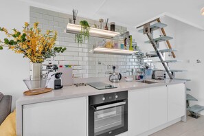 A modern kitchen with white cabinetry, a built-in oven, a coffee machine, and a hanging plant. - On the Water 7 Free Parking By My Getaways (Brighton)
