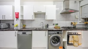 A modern kitchen with white cabinets, a dishwasher, a washing machine, a gas stove, and a stainless steel range hood. - Fully kitted, 4BR w/Parking, private Garden, Wi-Fi,Near City, Stadiums & Airport (Manchester)