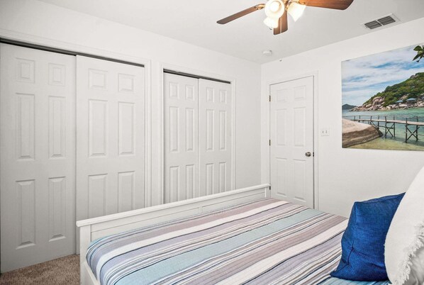 A bedroom with a bed, a ceiling fan, and a painting of a coastal scene.