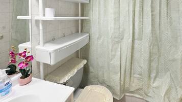 A bathroom with a toilet, a shelf, a sink, and a shower curtain.