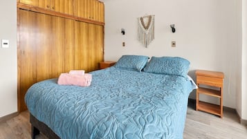A bedroom with a large bed, wooden wardrobe, two bedside tables, and wall-mounted decor.