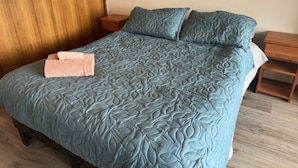A bed with a leaf-patterned quilt, a wooden nightstand, a wall-mounted macrame decoration, and a wooden floor. - Oceana Suites Ensenada Villarrica (Villarrica)