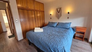 Un dormitorio con una cama grande, un armario de madera, dos luces fijadas a la pared y una mesita de noche.