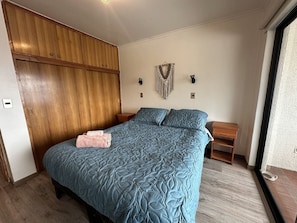 A bedroom with a large bed, wooden wardrobe, bedside tables, and a wall-mounted light fixture.
