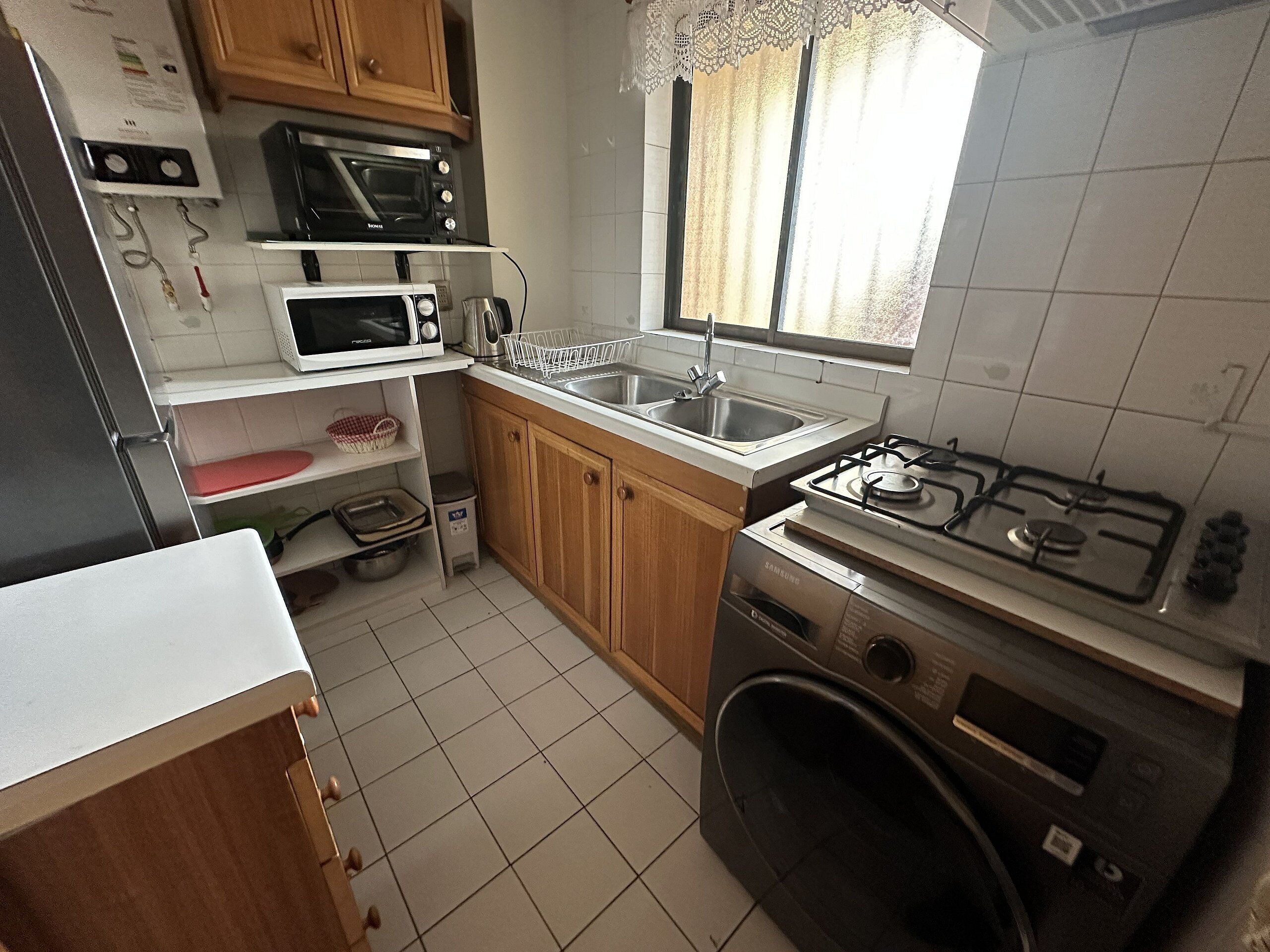 Cocina compacta con estufa a gas, microondas, pileta y muebles de madera.