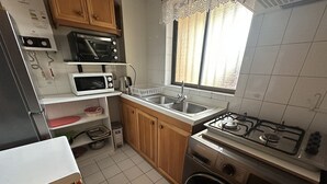 A compact kitchen with a gas stove, microwave, sink, and wooden cabinets. - Oceana Suites Ensenada Villarrica (Villarrica)