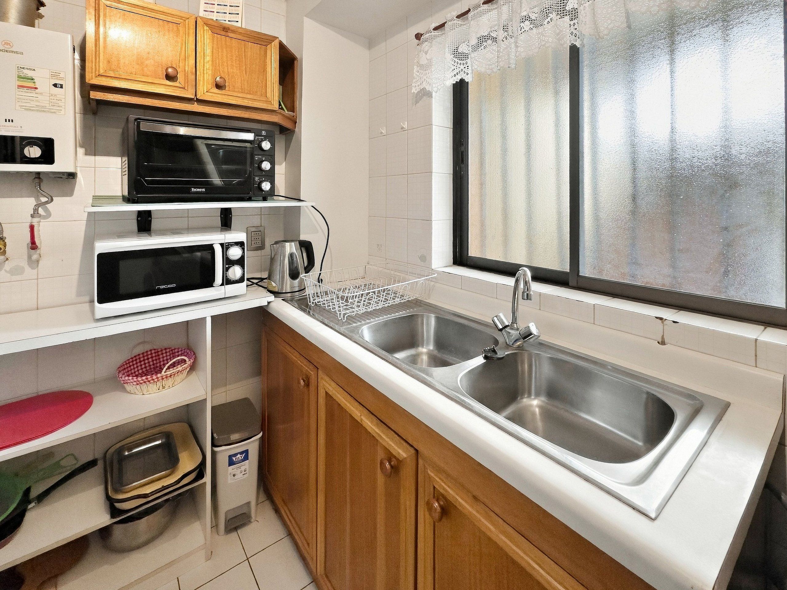 A compact kitchen with a double sink, a microwave, a toaster, and a kettle.